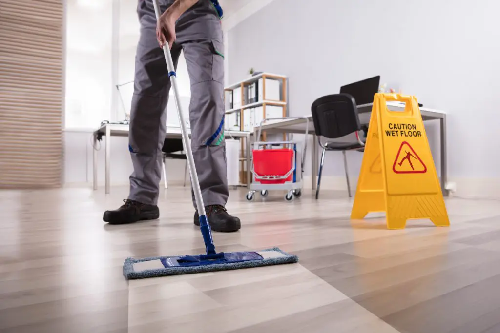Man with overalls cleaning a dirty floor with caution wet floor sign